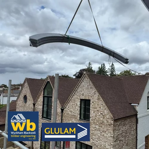 Glulam beam being lifted by crane over houses