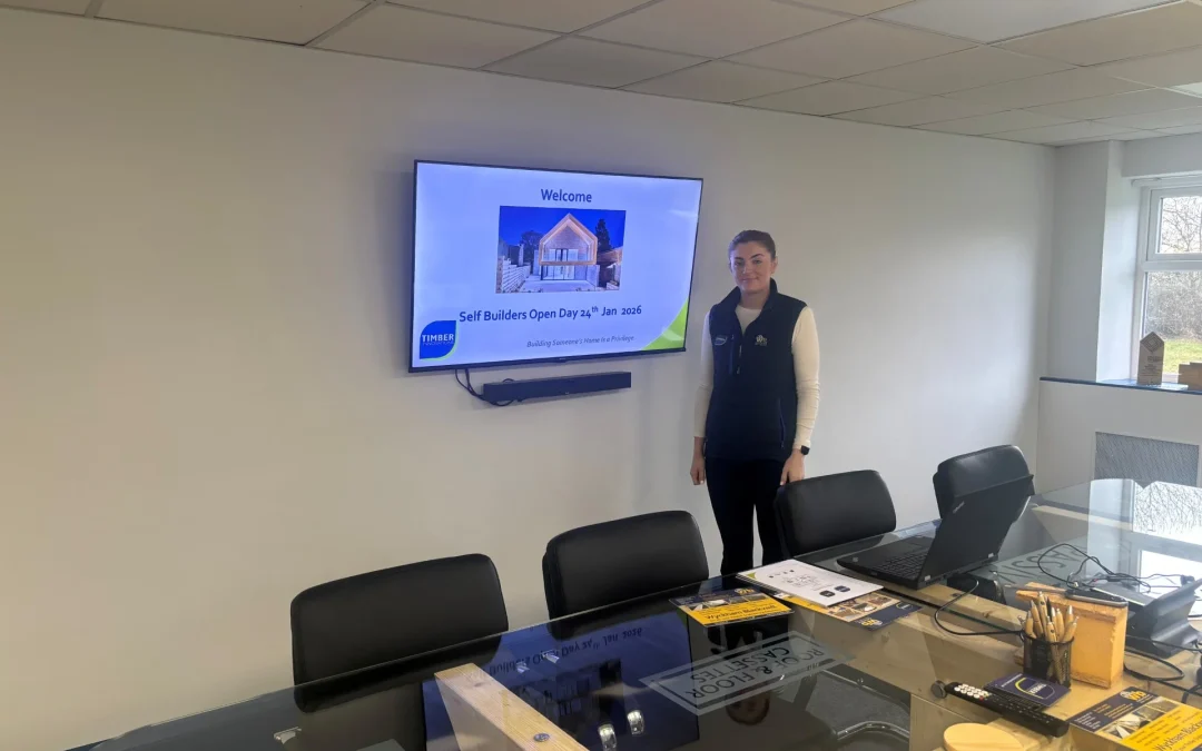 A lady standing in front of a screen with the Self Build Workshop details on a TV screen.