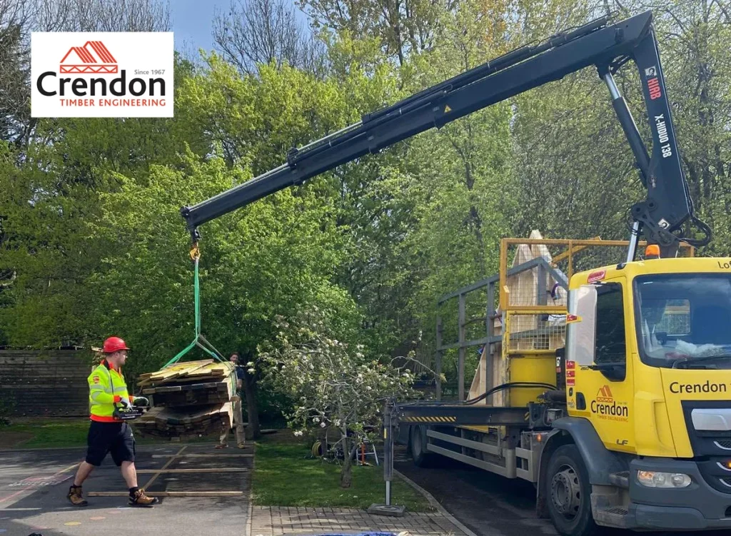 Crendon yellow lorry with a crane moving timber with a man walking towards it in a yellow high vis and red hard hat