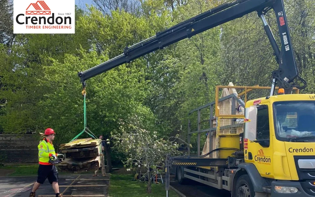 Crendon yellow lorry with a crane moving timber with a man walking towards it in a yellow high vis and red hard hat