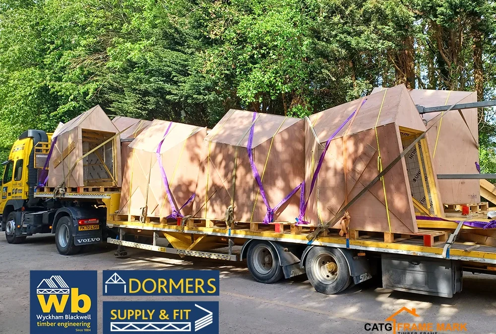 Wyckham Blackwell flatbed truck carrying multiple prefabricated wooden Dormer units strapped with purple webbing.