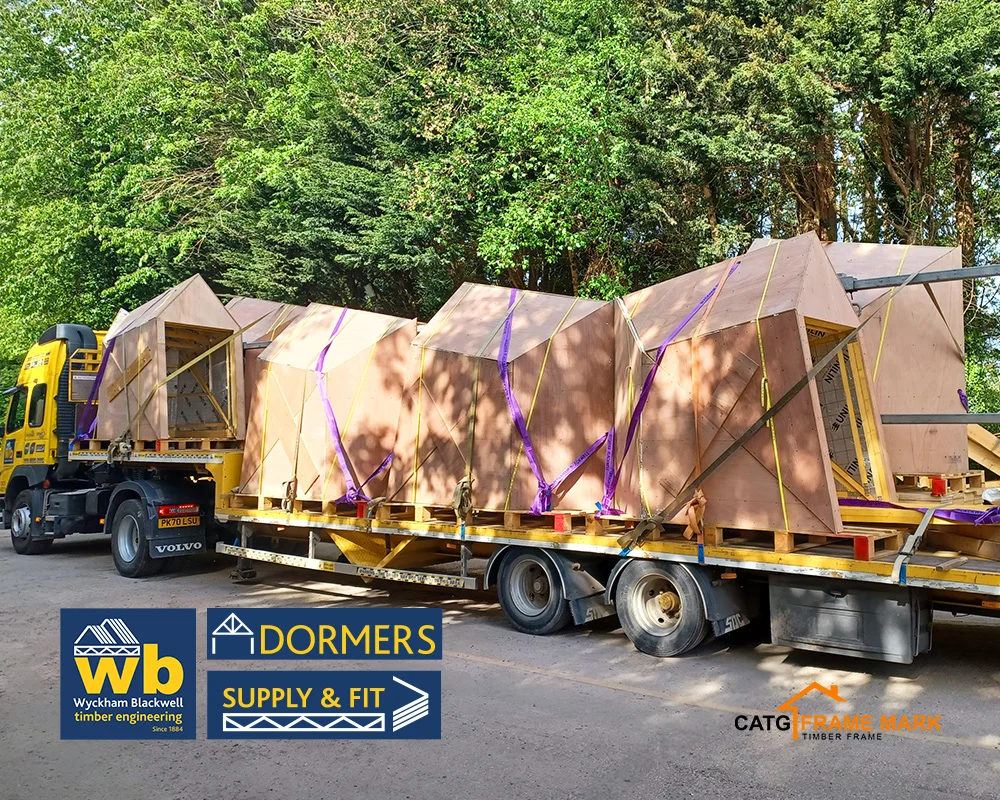 Wyckham Blackwell flatbed truck carrying multiple prefabricated wooden Dormer units strapped with purple webbing.