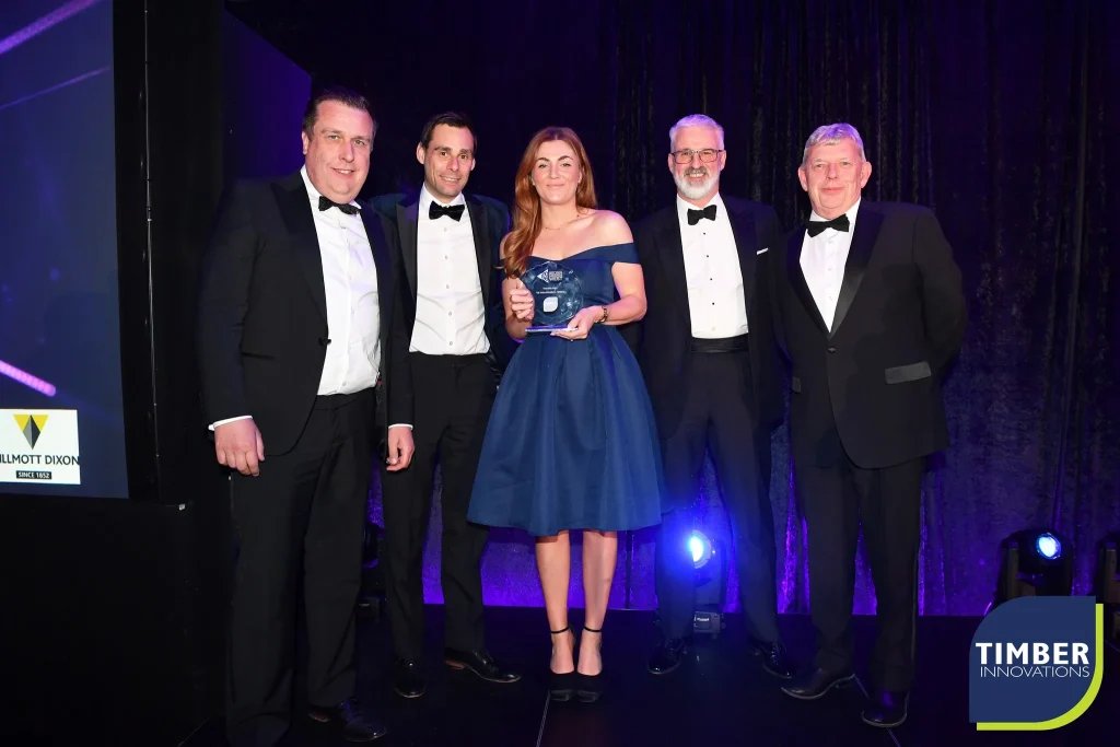 4 men in suits and 1 woman in a blue dress standing on a stage holding a trophy