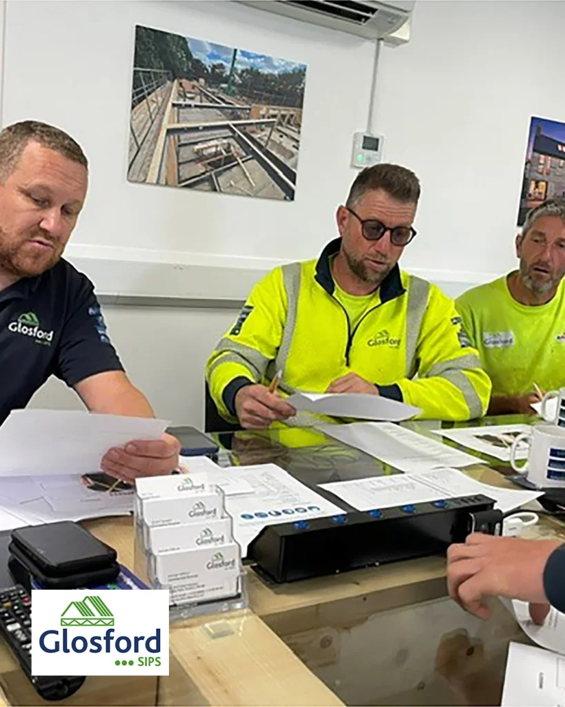 Three construction workers in high-visibility Glosford shirts reviewing paperwork around a table during a site meeting.