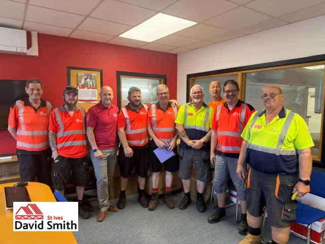 Nine workers in high-visibility vests and shirts standing in an office beside a David Smith St Ives logo.