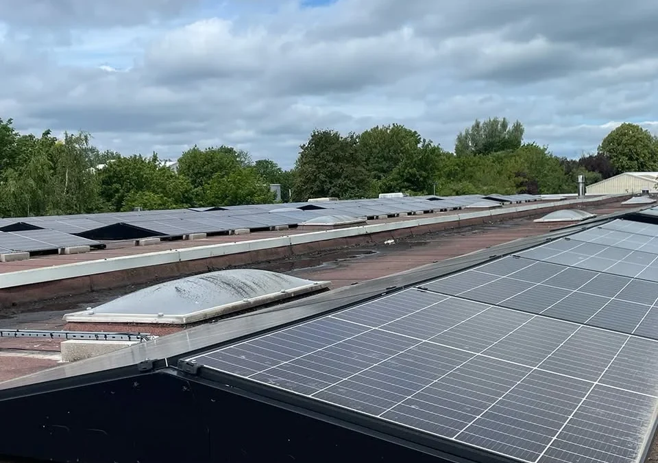 Multiple rows of rooftop solar panels on a commercial roof, trees and buildings in the background, Timber Innovations logo.
